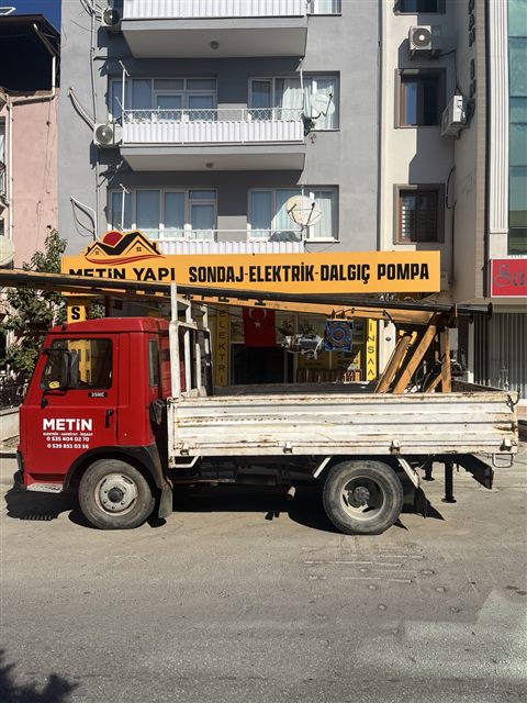 İşletme önünde, kasasında sondaj ekipmanı bulunan kırmızı Metin Yapı iş aracı
