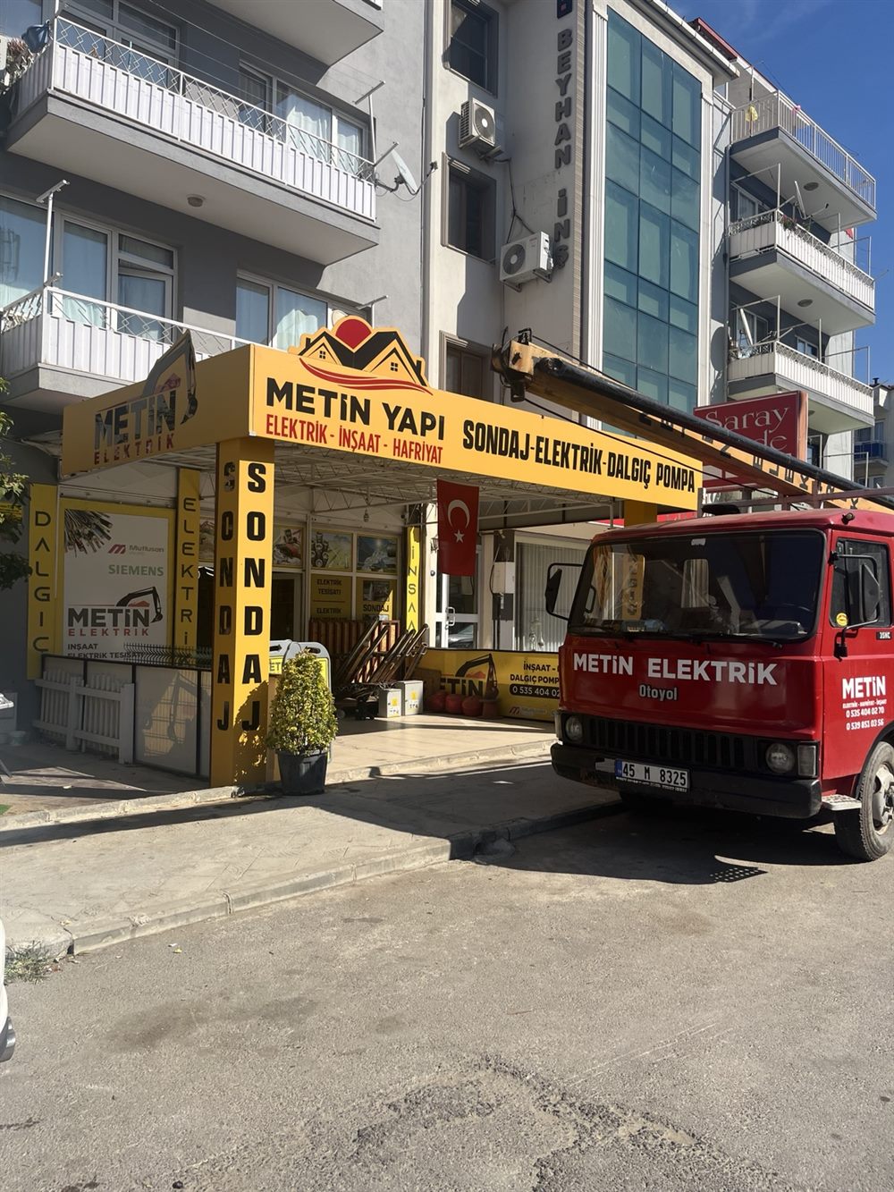 Metin Yapı'nın sarı tabelası, işletme girişi ve önündeki kırmızı iş aracı